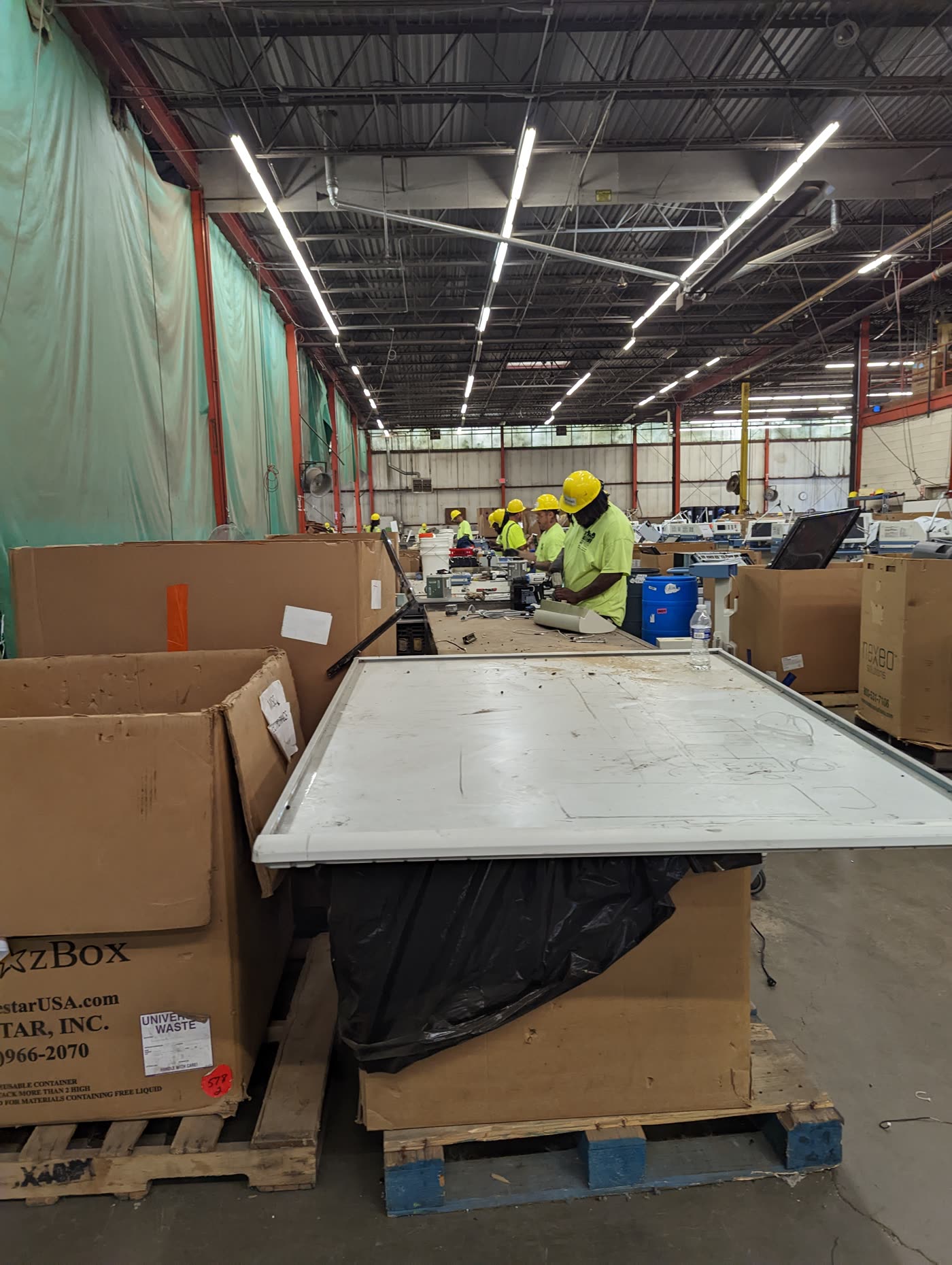 The RecycleForce plant floor in Indianapolis: workers in hard hats dismantling electronics at long benches, with pallets of sorted equipment in the foreground